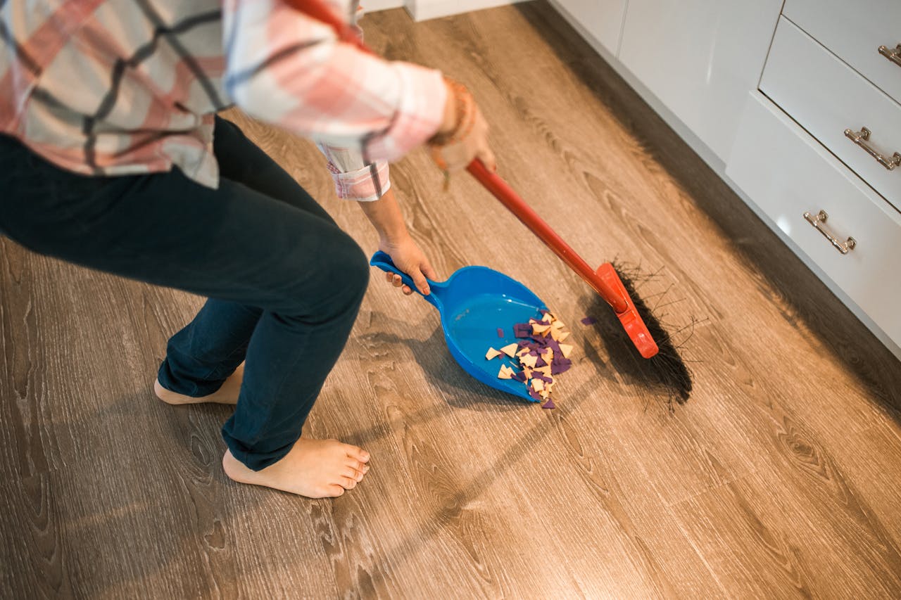 Close-up of a person sweeping debris into a blue dustpan on a wooden floor.